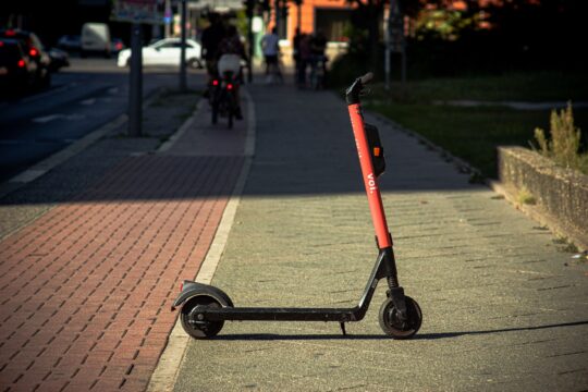 E-scooter accident lawsuit who is liable (A Voi e-scooter parked on a sunlit city sidewalk with a blurred urban background.)