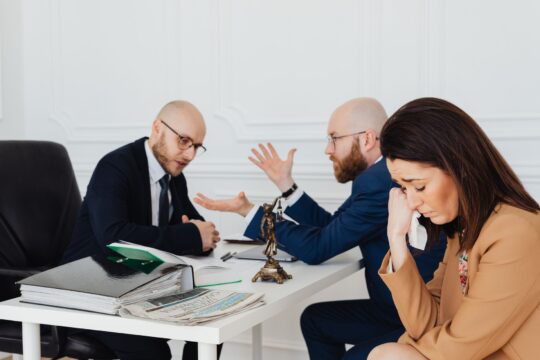 Medical malpractice lawyer (A woman appears distressed while two lawyers converse in an office.)