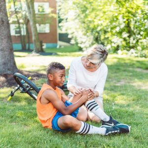 Bicycle accident lawyer (A woman comforts an injured child beside a bicycle in a sunny park setting.)