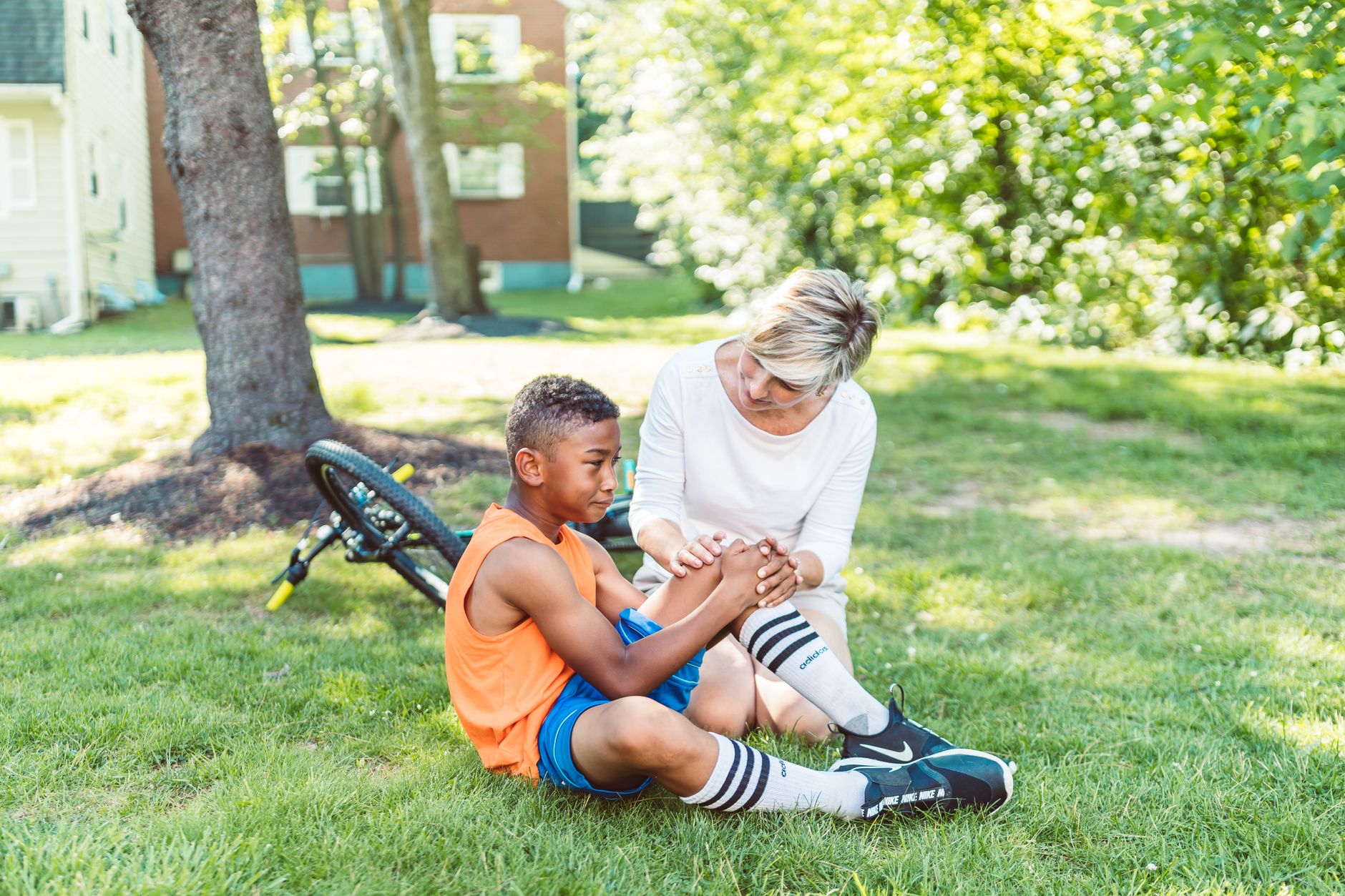 Bicycle accident lawyer (A woman comforts an injured child beside a bicycle in a sunny park setting.)