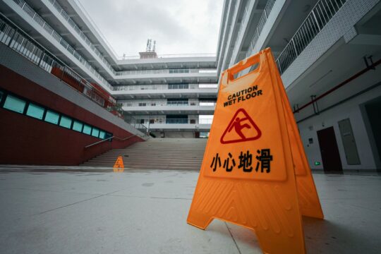 Premises liability lawyer (Yellow caution wet floor sign in a modern building courtyard with overcast sky.)