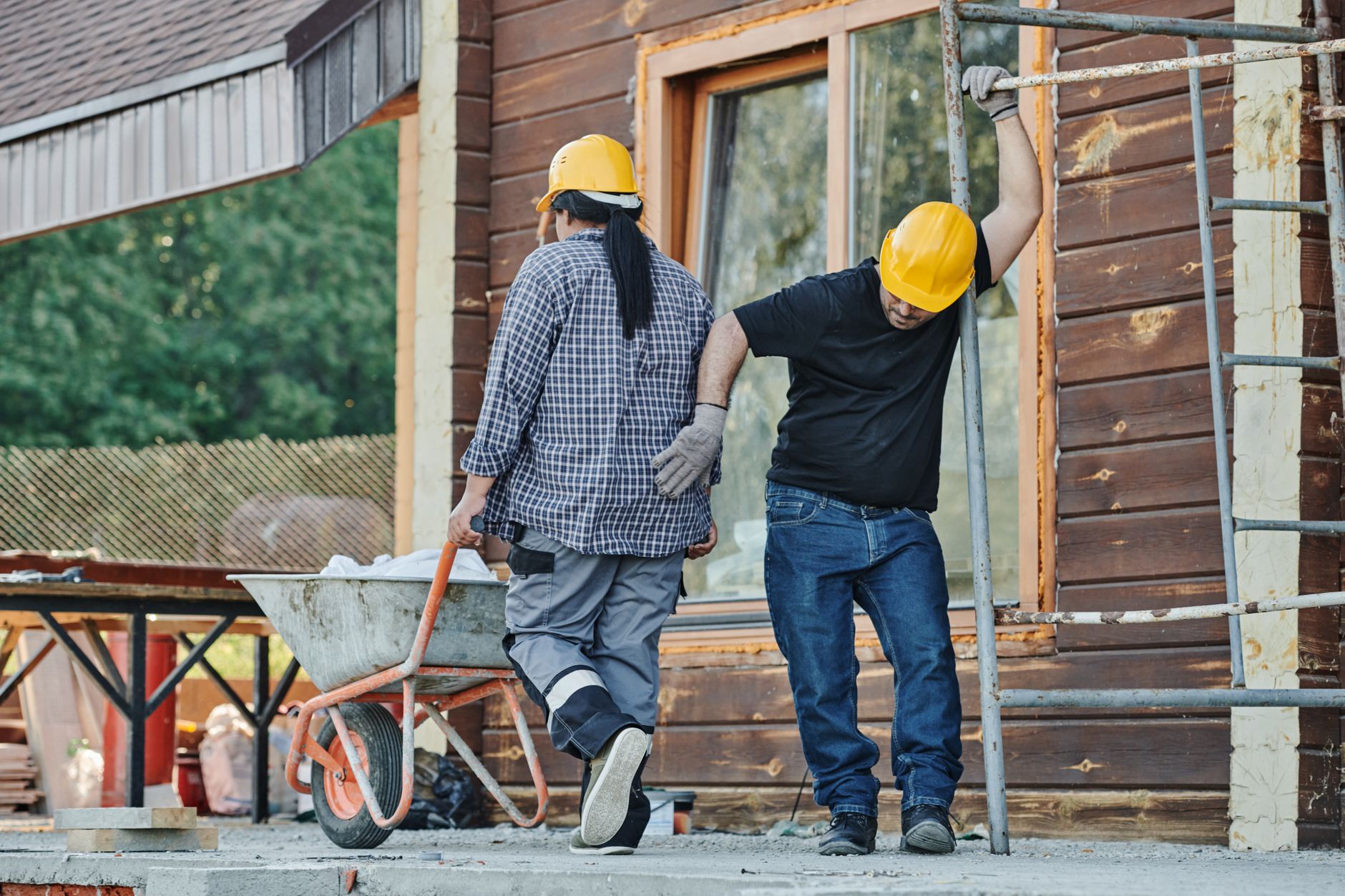 Workers comp benefits (Two construction workers wearing hard hats work at an outdoor site, one with a wheelbarrow.)