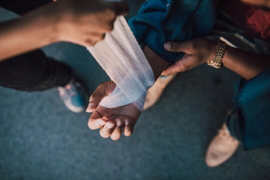 Burn injury lawyer (A detail shot showing hands applying a bandage to an injured wrist outdoors.)